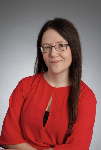 Headshot of Kristen. She has long brown hair. She is wear a red top and glasses.  She is smiling. 