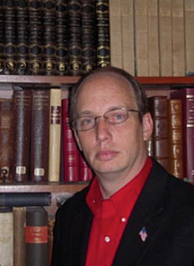 Brian Price in a red shirt in front of a bookcase.