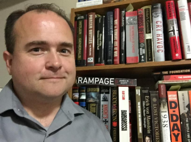 Cody Carlson standing to the side of a bookcase.