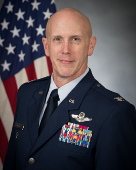 Jeremy Reeves in USAF dress unifrom standing in front of an American Flag, USAF professional profile.
