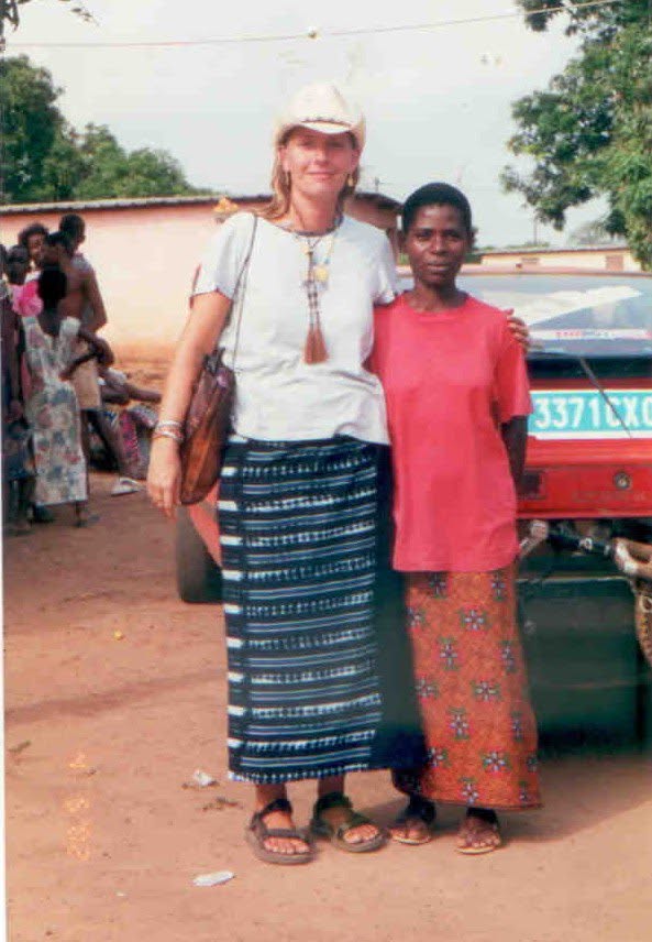 Annaliese and Rosalie stand facing the camera. Annaliese is wearing a dress and hat while Rosalie is wearing a pink shirt and patterened dress.