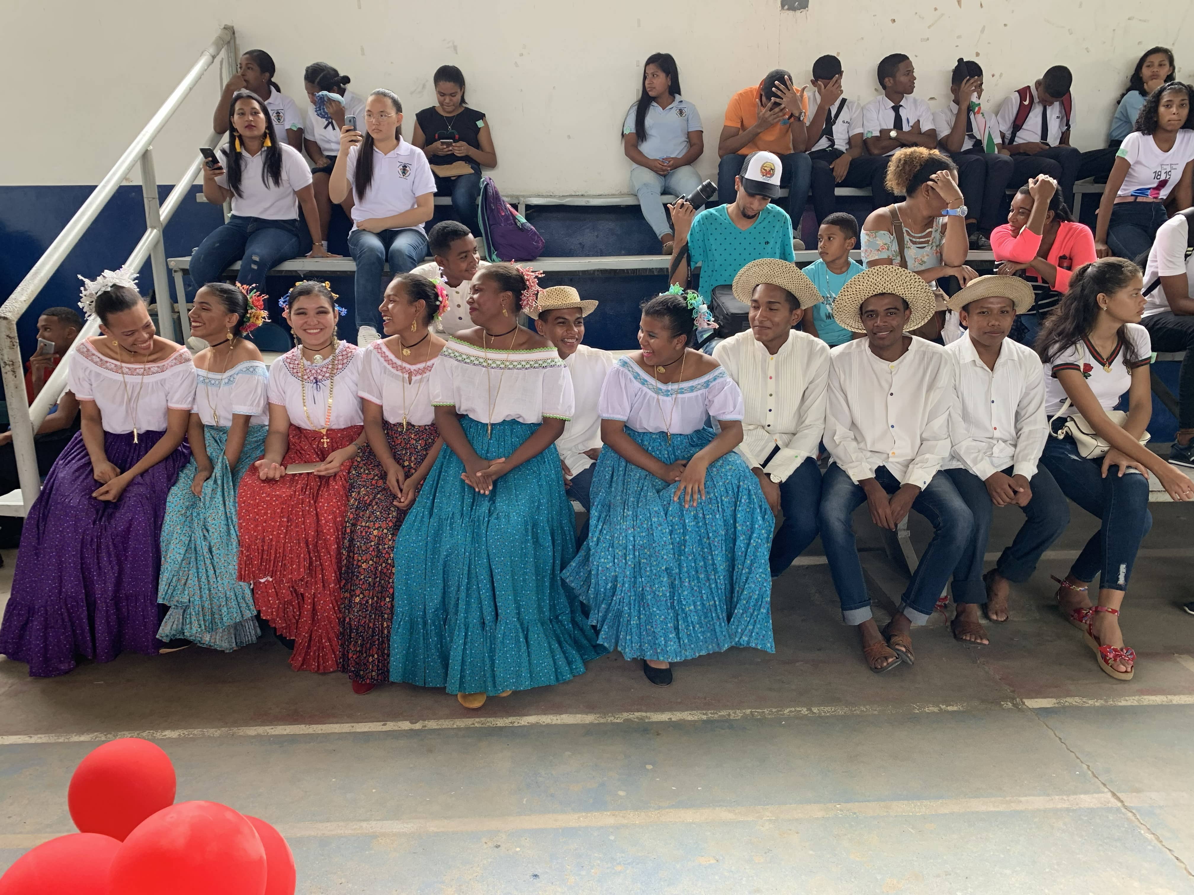 High school students sit on bleachers in traditional Panama outfits.