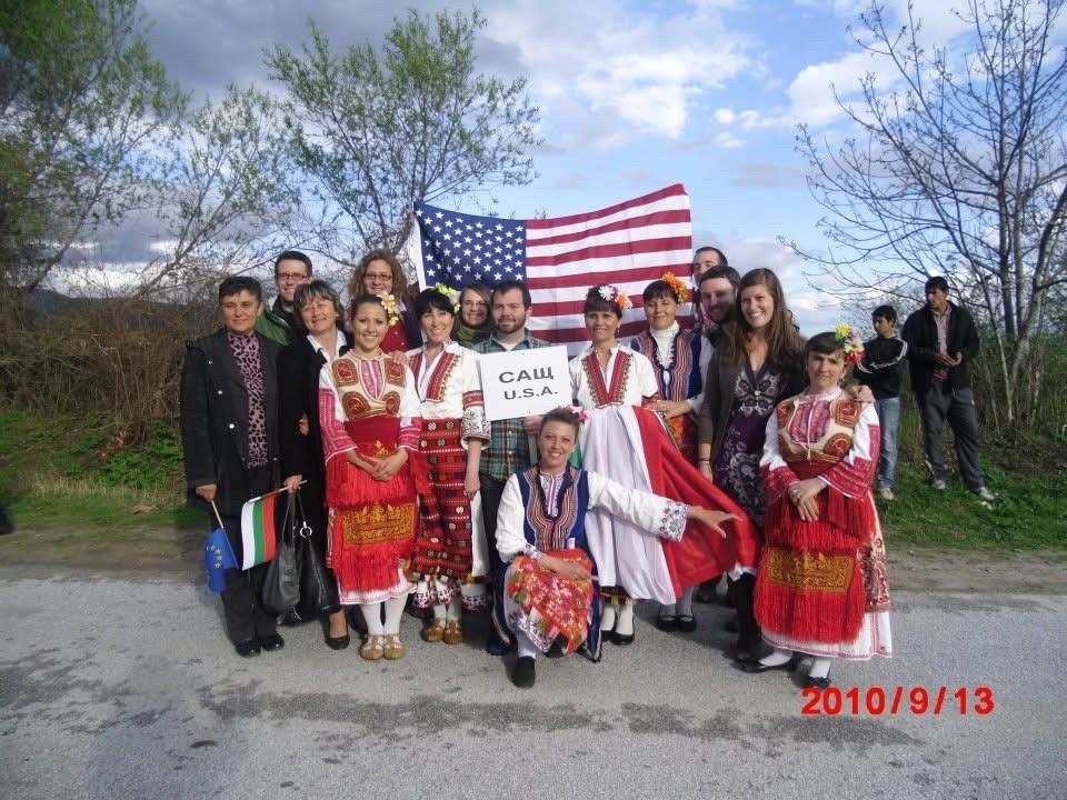 Katie Van Natta poses with Bulgarian Host Country Nationals in front of a US flag.