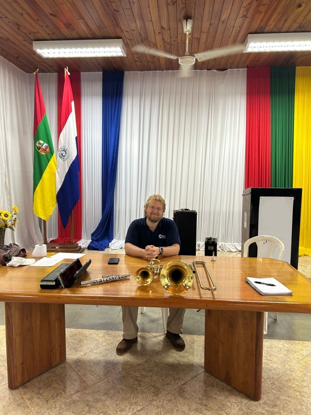 Lee sits at a large table with the Paraguay flag behind him and two musical instruments on the table.