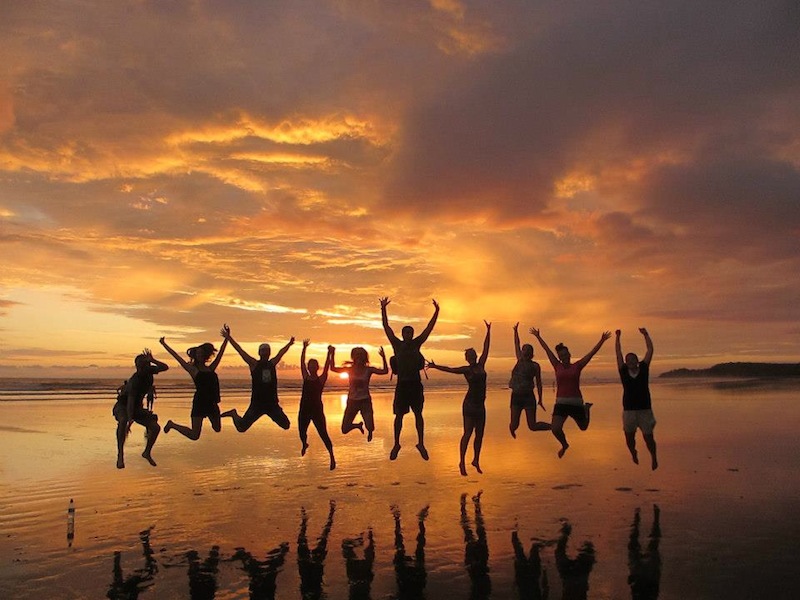 A group of Peace Corps Volunteers jumping in the air in front of a bright orange sunset.