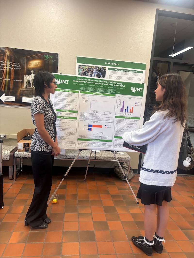 Researcher speaking to student about the research poster they are standing next to 